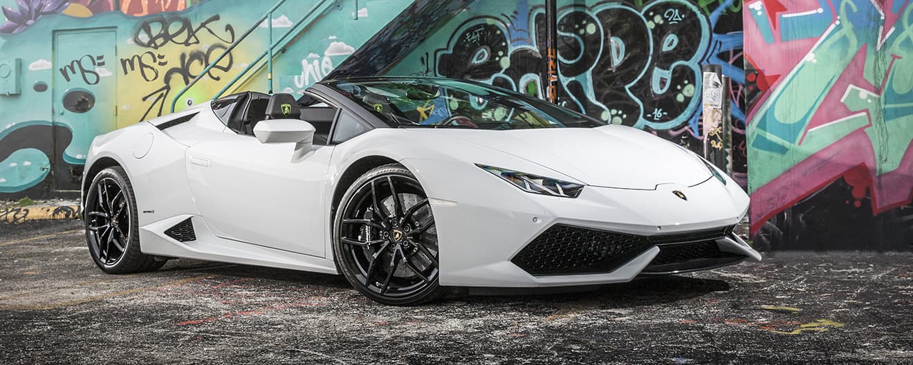 Front three-quarter view of a white Lamborghini Huracán Spyder parked before a graffiti-covered wall. 